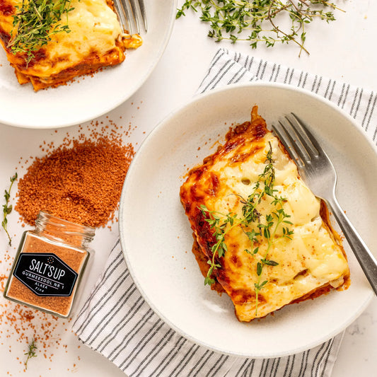 Gourmet lasagna topped with fresh herbs, fork, and Alaea fine salt on Spice n Slice Market.