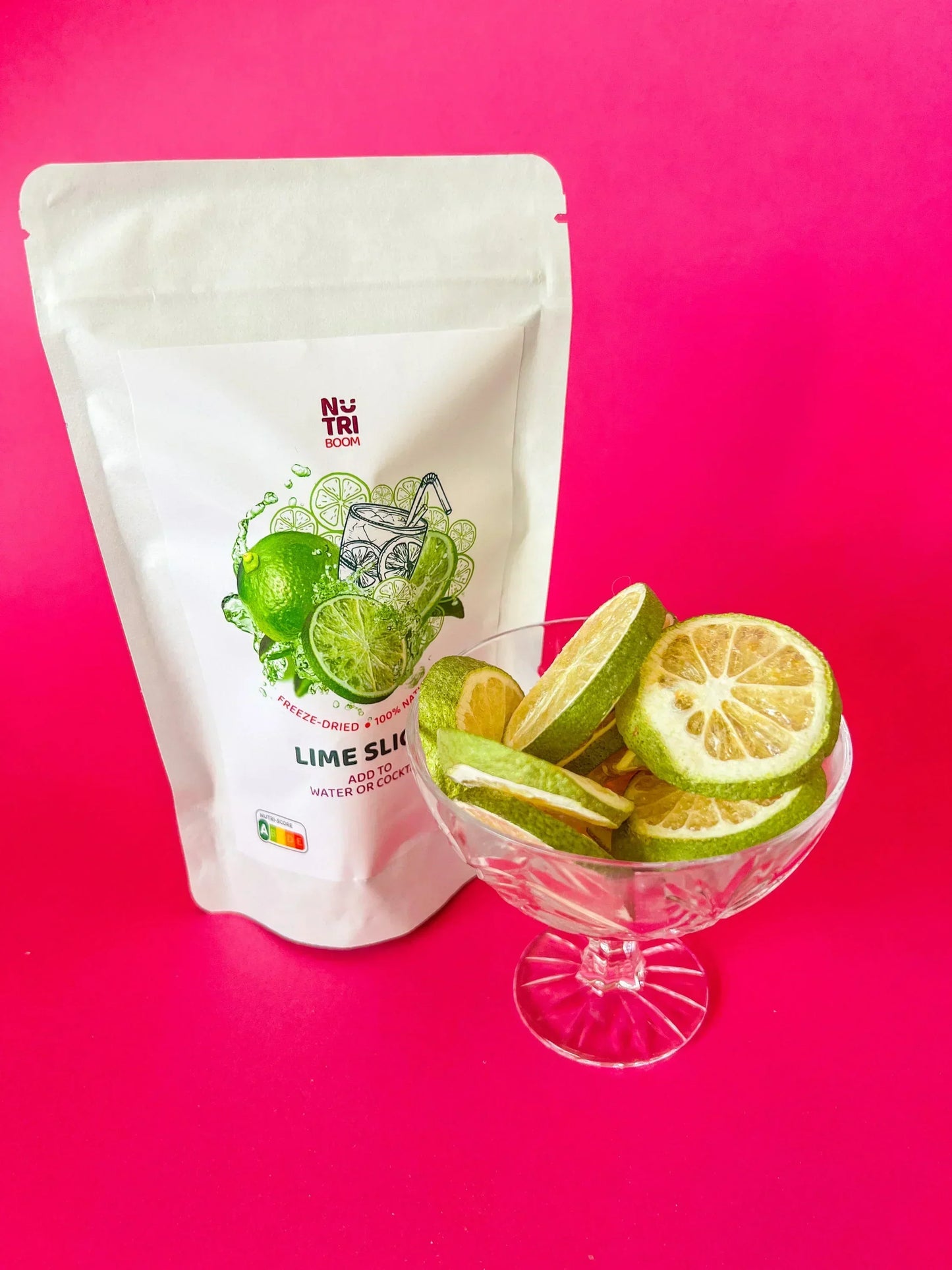 Freeze-dried lime slices in glass bowl with Nutri Boom packaging, pink background, Spice n Slice Market