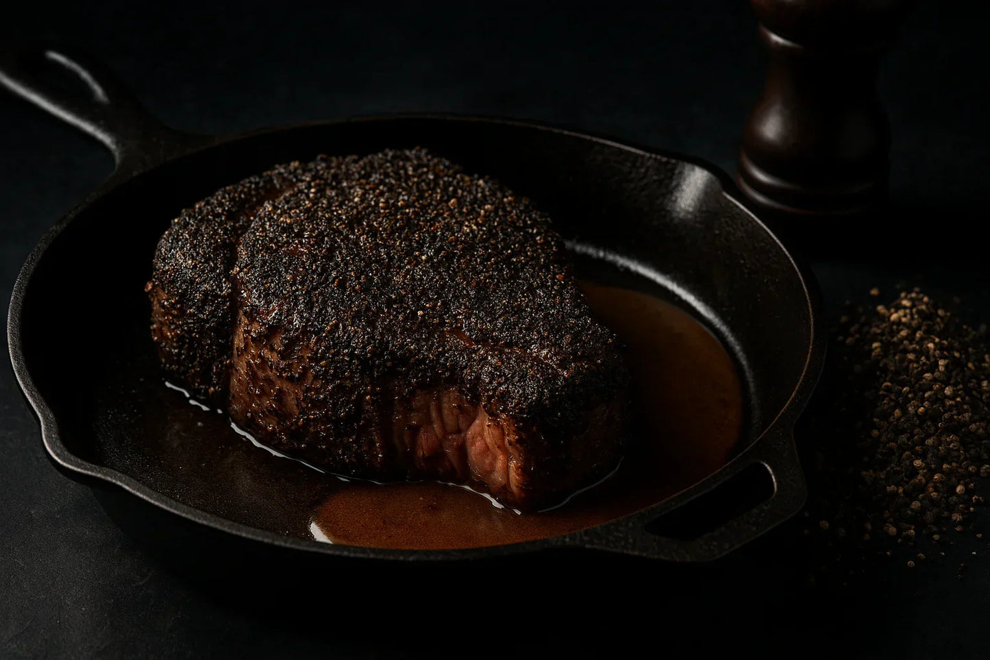 Pepper-crusted steak in cast iron pan with black pepper and pan sauce