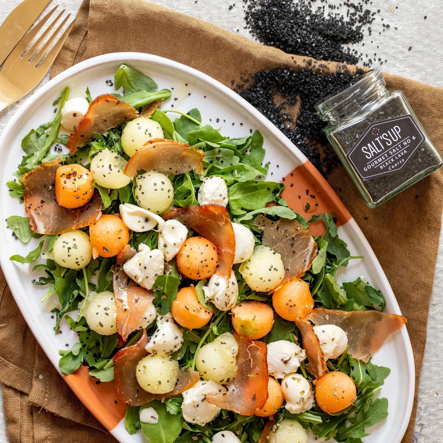 Fresh arugula salad with melon balls, mozzarella, cured meat, and coarse black lava salt