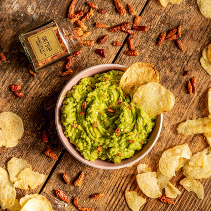 Guacamole with potato chips, dried chili flakes, and gourmet spice jar on rustic wood table
