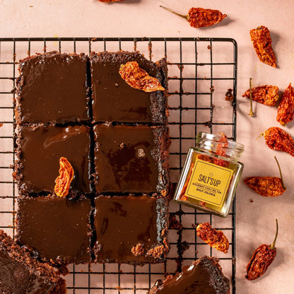 Chocolate brownies with Bhut Jolokia dried chili, gourmet chili jar, and whole dried chilies on a cooling rack.