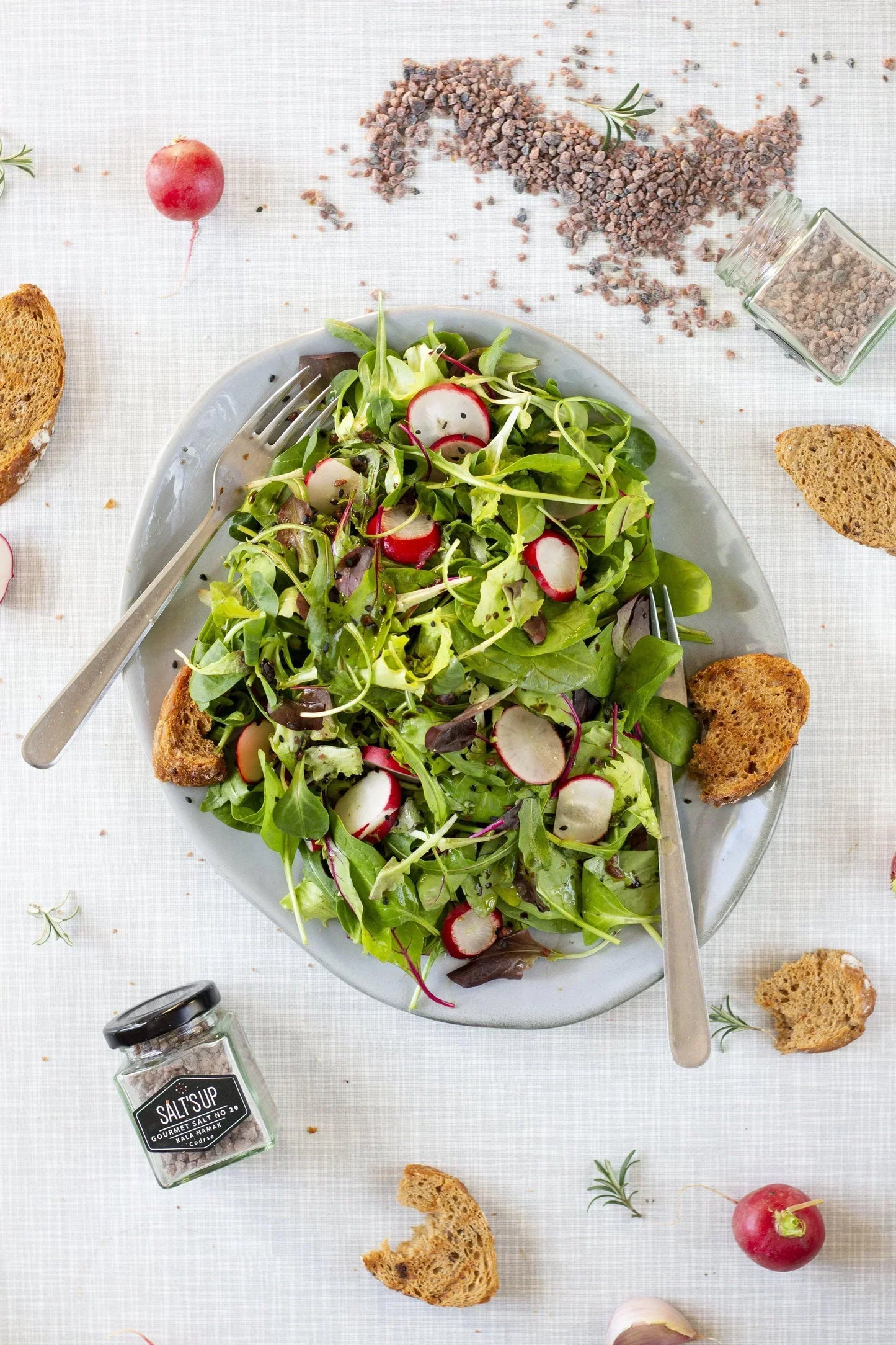 Fresh green salad with sliced radishes, coarse kala namak salt, artisan bread, and Salt's Up jar