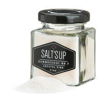 Glass jar of Salt'sUp Crystal Pink fine gourmet salt with a small salt pile beside it