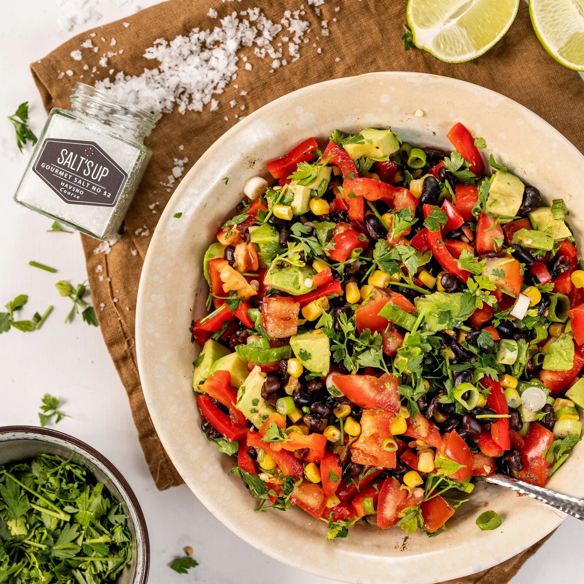Fresh avocado, tomato, corn, and black bean salad in bowl with Salt's Up gourmet salt, herbs, and lime