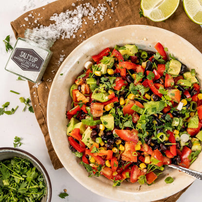 Fresh avocado, tomato, corn, and black bean salad in bowl with Salt's Up gourmet salt, herbs, and lime