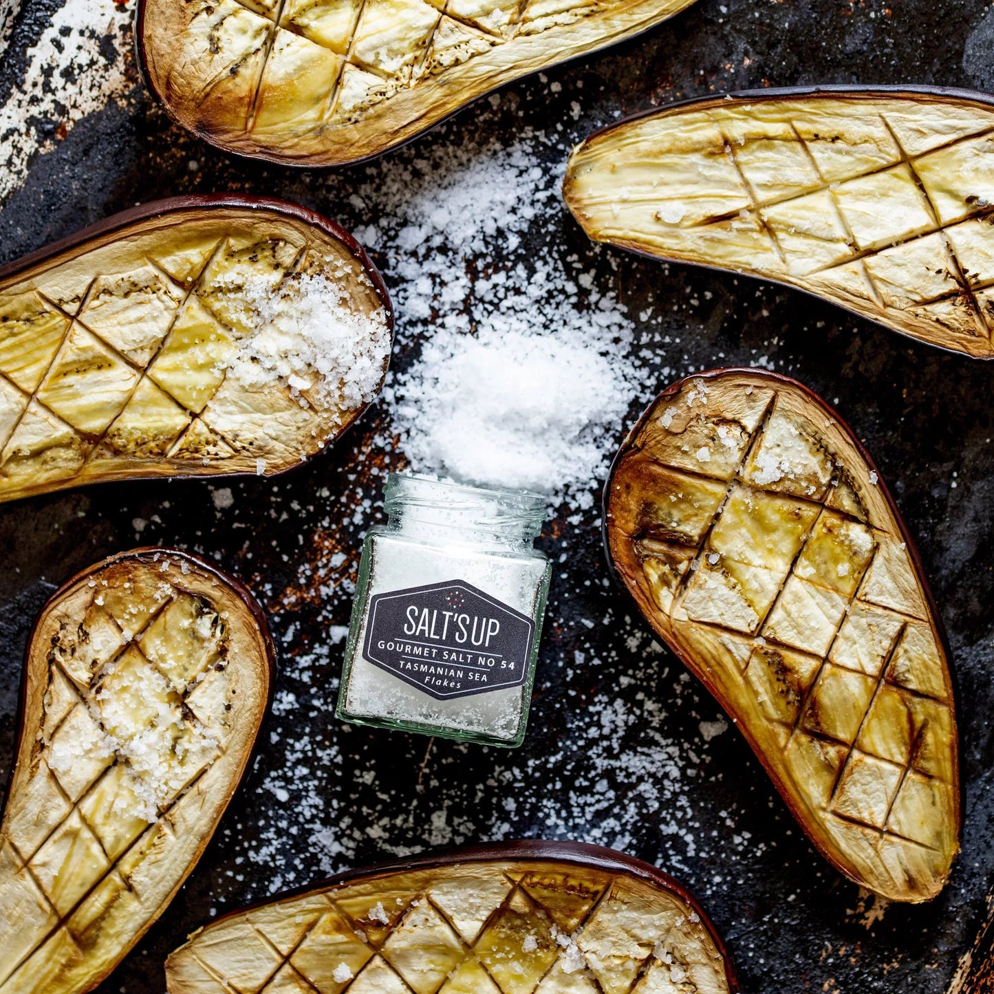 Roasted eggplant halves with sea salt flakes and a jar of Tasmanian sea salt on a baking tray