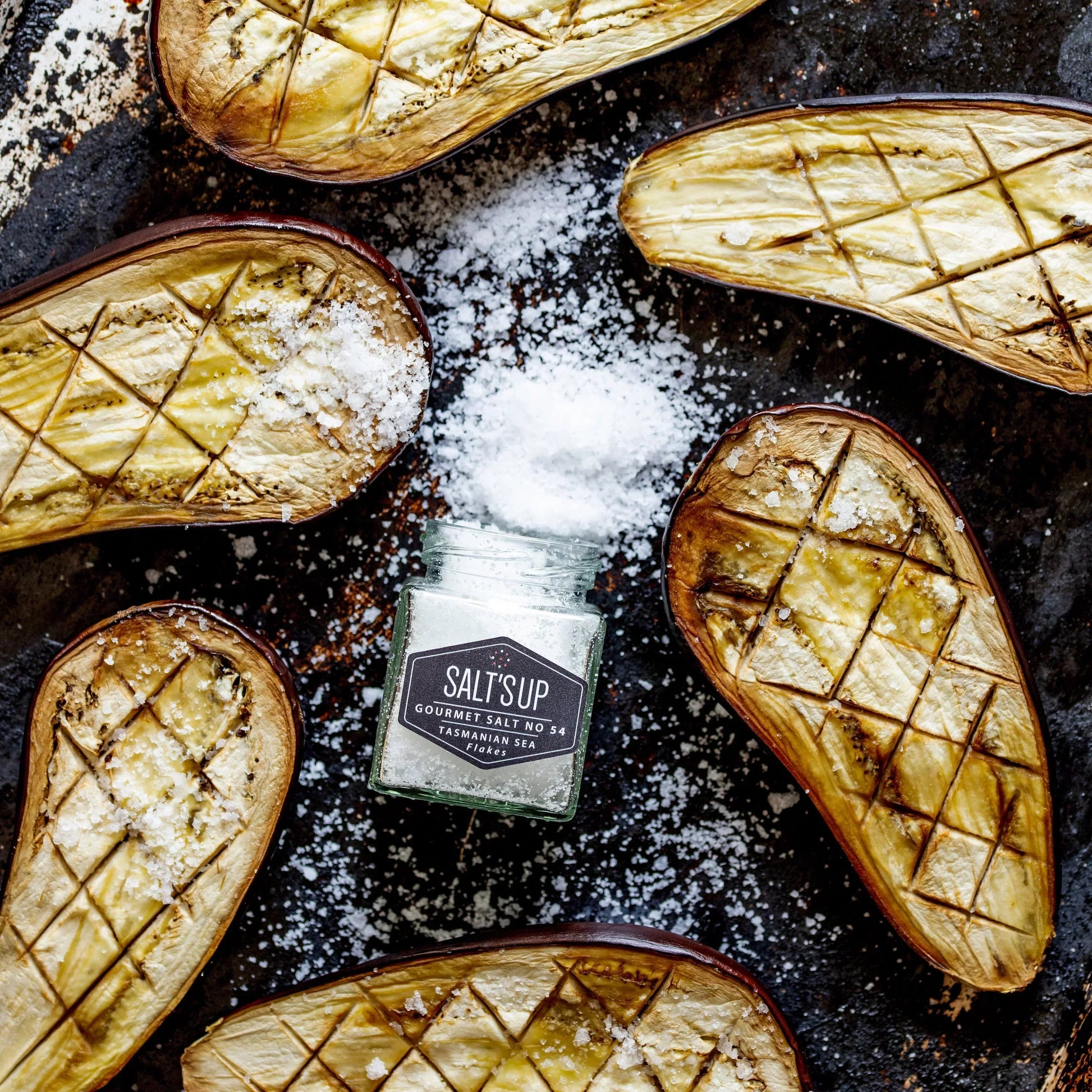 Roasted eggplant halves with sea salt flakes and a jar of Tasmanian sea salt on a baking tray