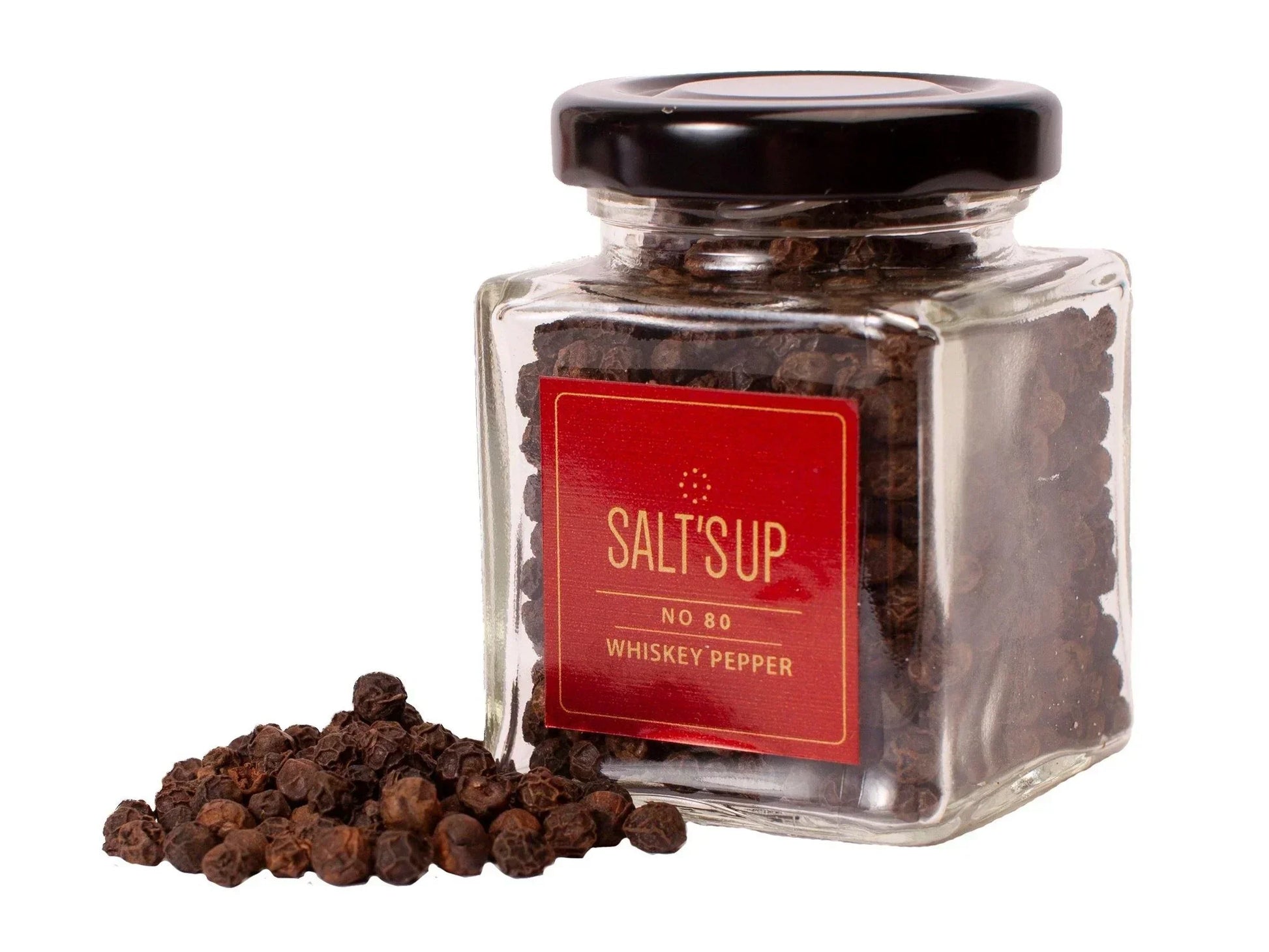 Glass jar of whiskey peppercorns with a black lid and loose peppercorns beside it