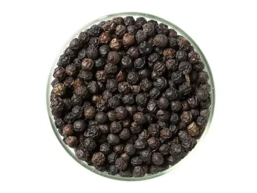 Glass bowl filled with whole black Kampot peppercorns on white background
