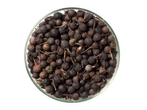 Whole dried cubeb pepper berries in a glass bowl on white background