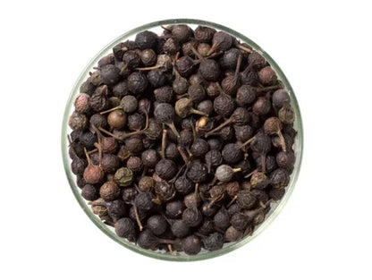 Whole dried cubeb pepper berries in a glass bowl on white background