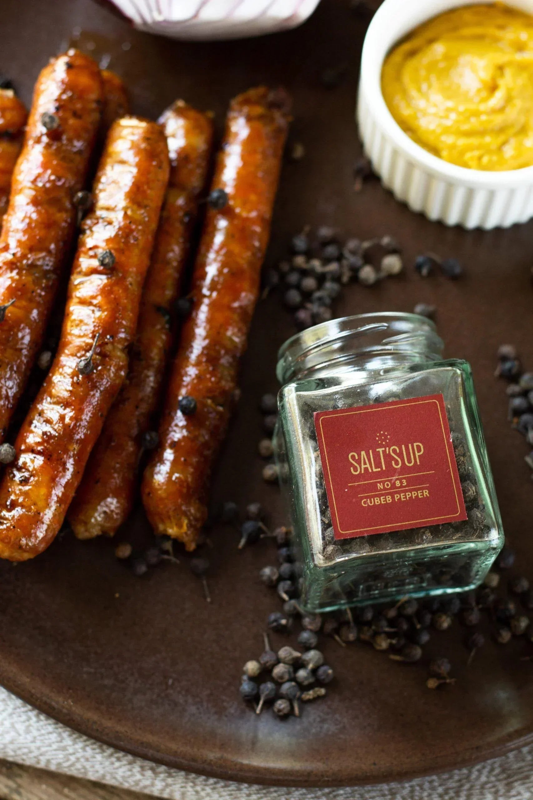 Cubeb pepper sausages, cubeb peppercorns, and mustard dip on rustic plate at Spice n Slice Market