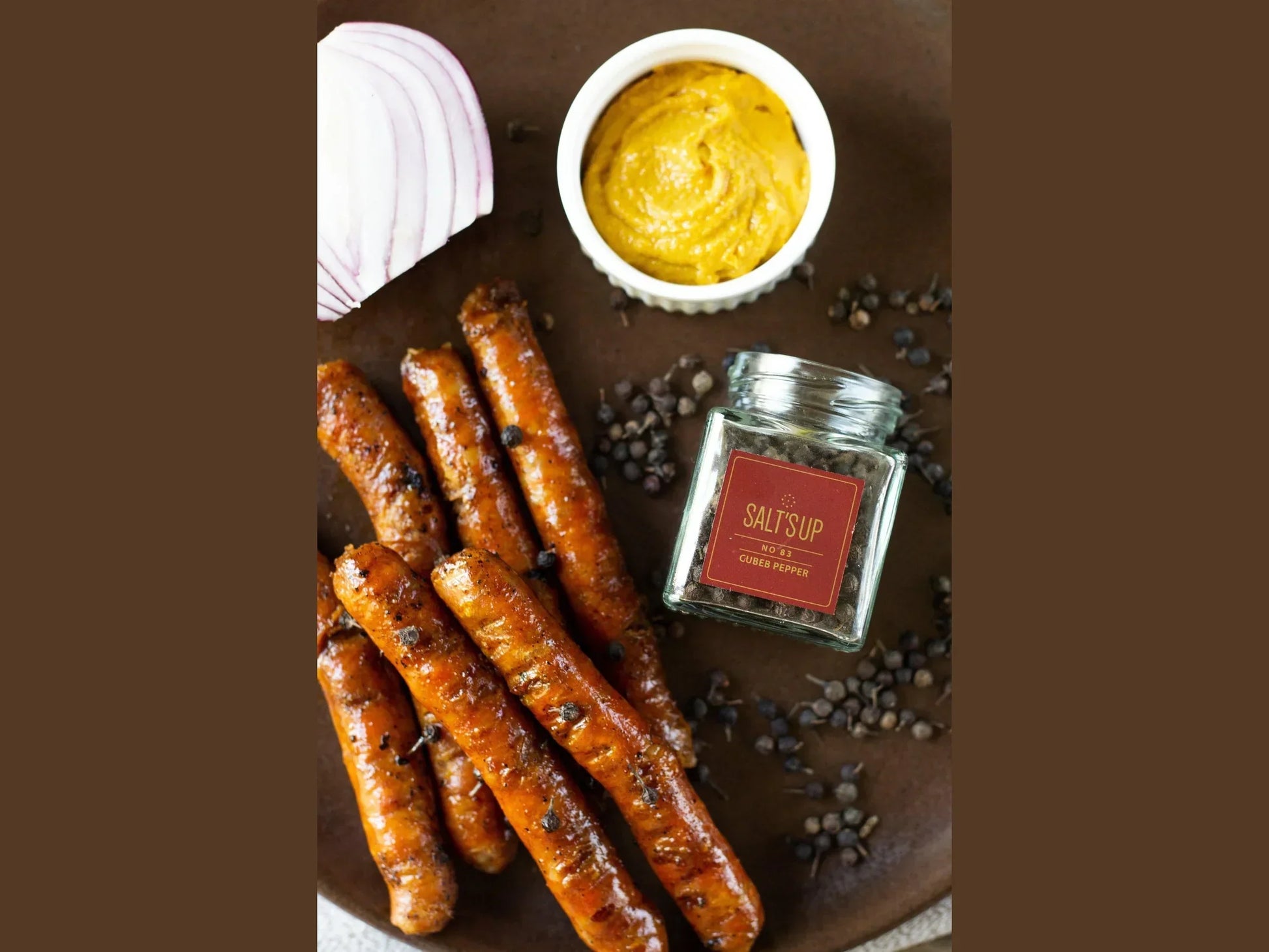 Grilled sausages with cubeb pepper, mustard dip, sliced red onion, and peppercorn jar
