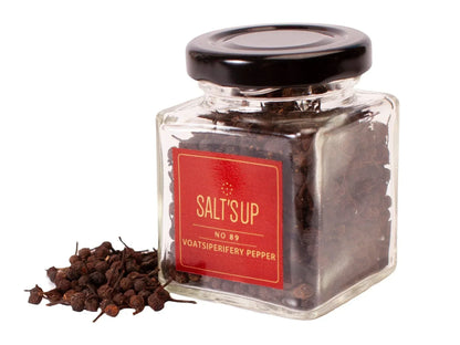 Glass jar of Voatsiperifery pepper with black lid and peppercorns scattered