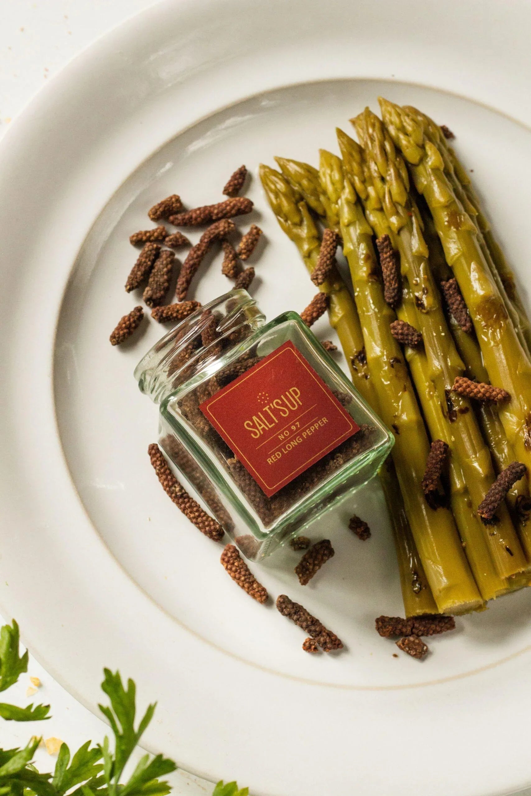 Jar of red long pepper and cooked asparagus spears on a white plate