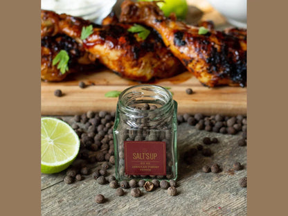 Jamaican pimento pepper jar with whole peppercorns, grilled chicken, and lime on rustic table