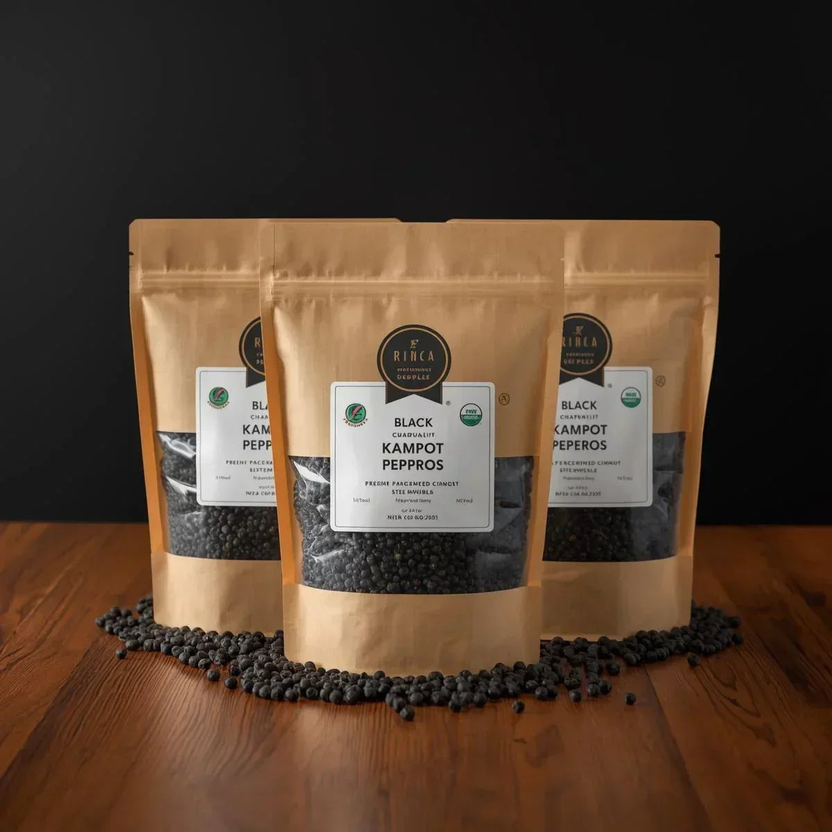 Three brown stand-up pouches of Rinka Black Kampot Peperos on wood surface with black peppercorns scattered around