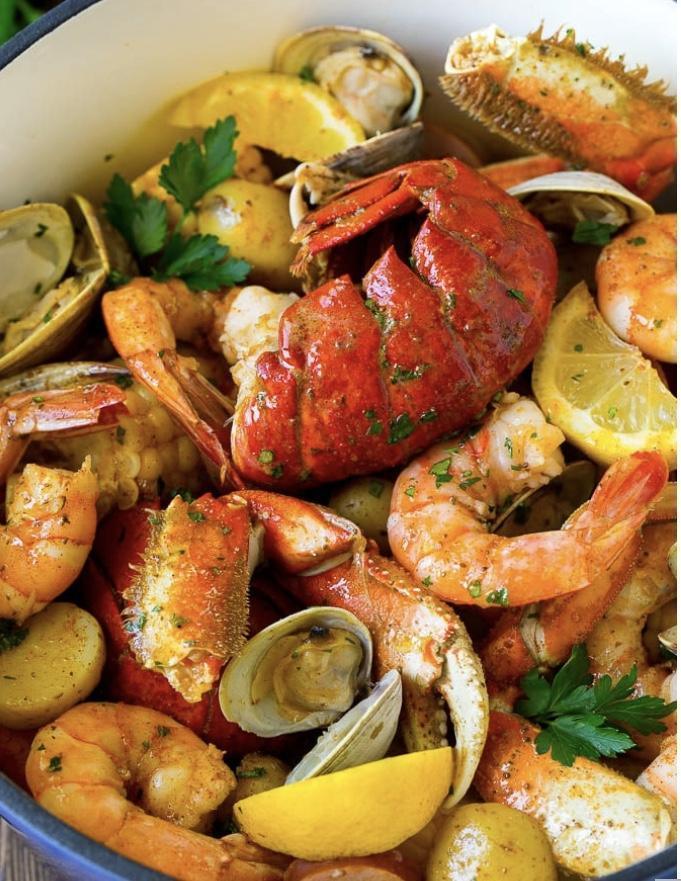Seafood boil with lobster, shrimp, crab, clams, potatoes, lemon wedges, and herbs