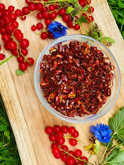 Glass bowl of dried Kampot pepper ribbons on wooden board with fresh red currants and blue flowers