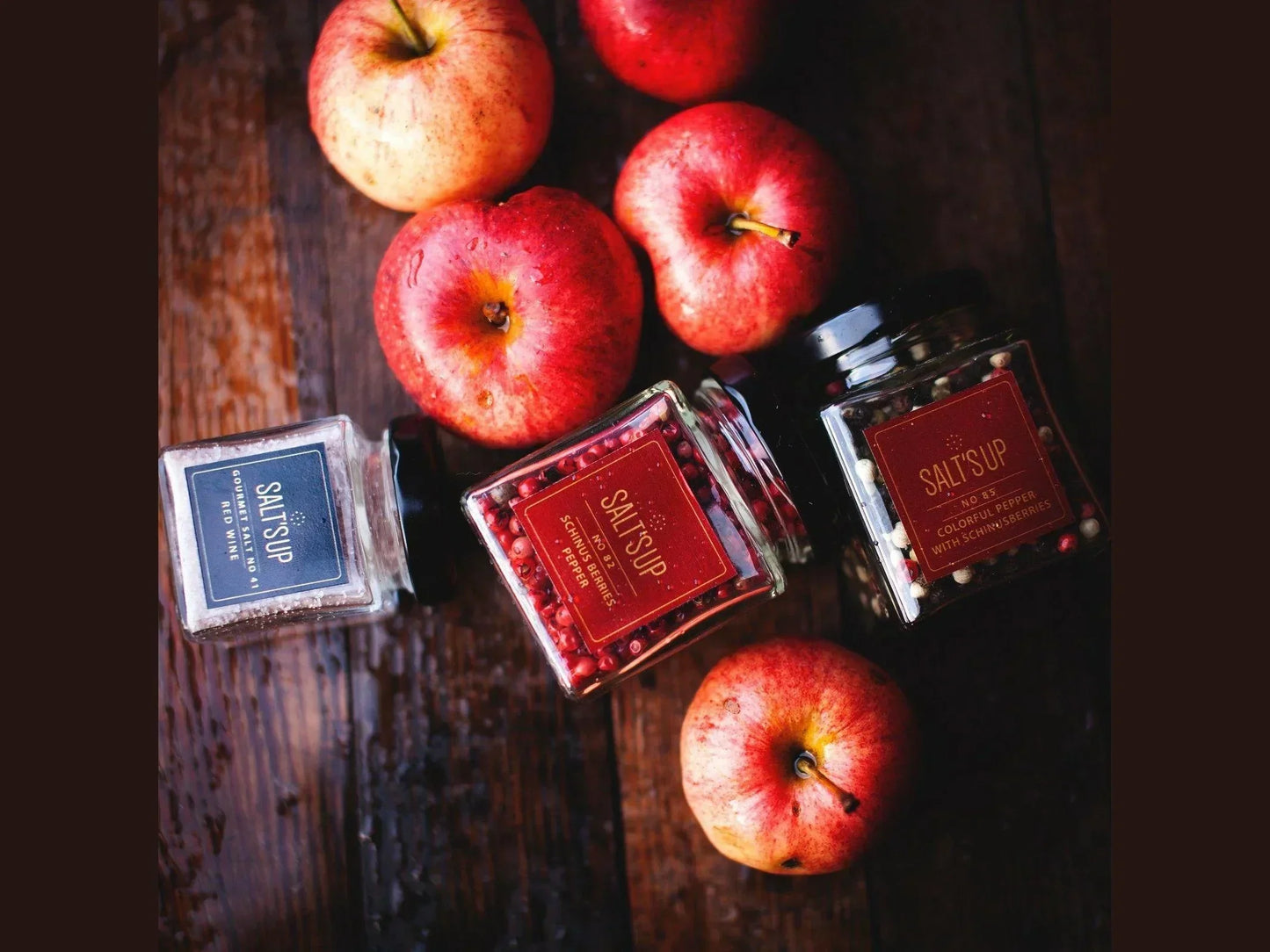 Jars of colorful peppercorns and seasoning with red apples on rustic wooden table