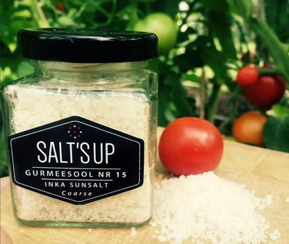Jar of coarse Inka sun salt on wood board with tomatoes and green garden background
