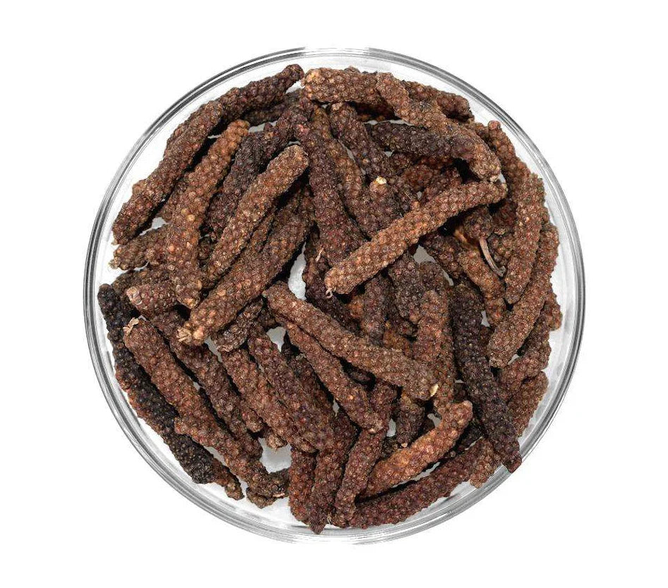 Whole long peppercorns in a clear glass bowl on a white background