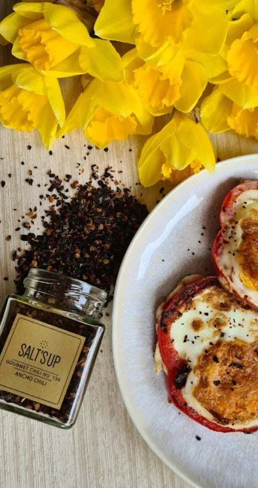 Gourmet ancho chili seasoning, baked stuffed tomatoes, yellow daffodils on wood table.