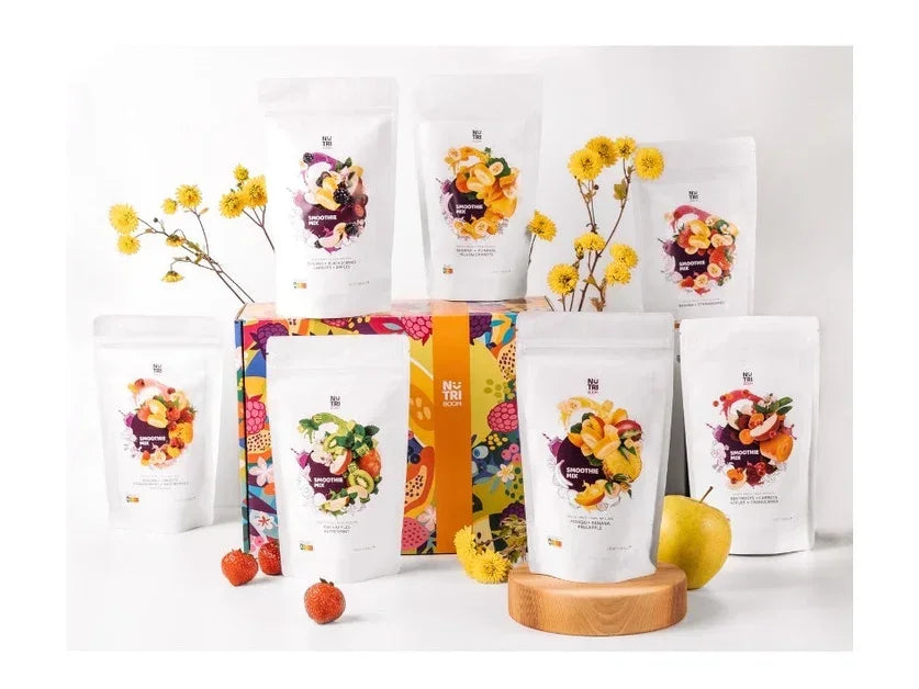 Assorted freeze-dried smoothie packs with mixed fruits displayed near colorful box and flowers