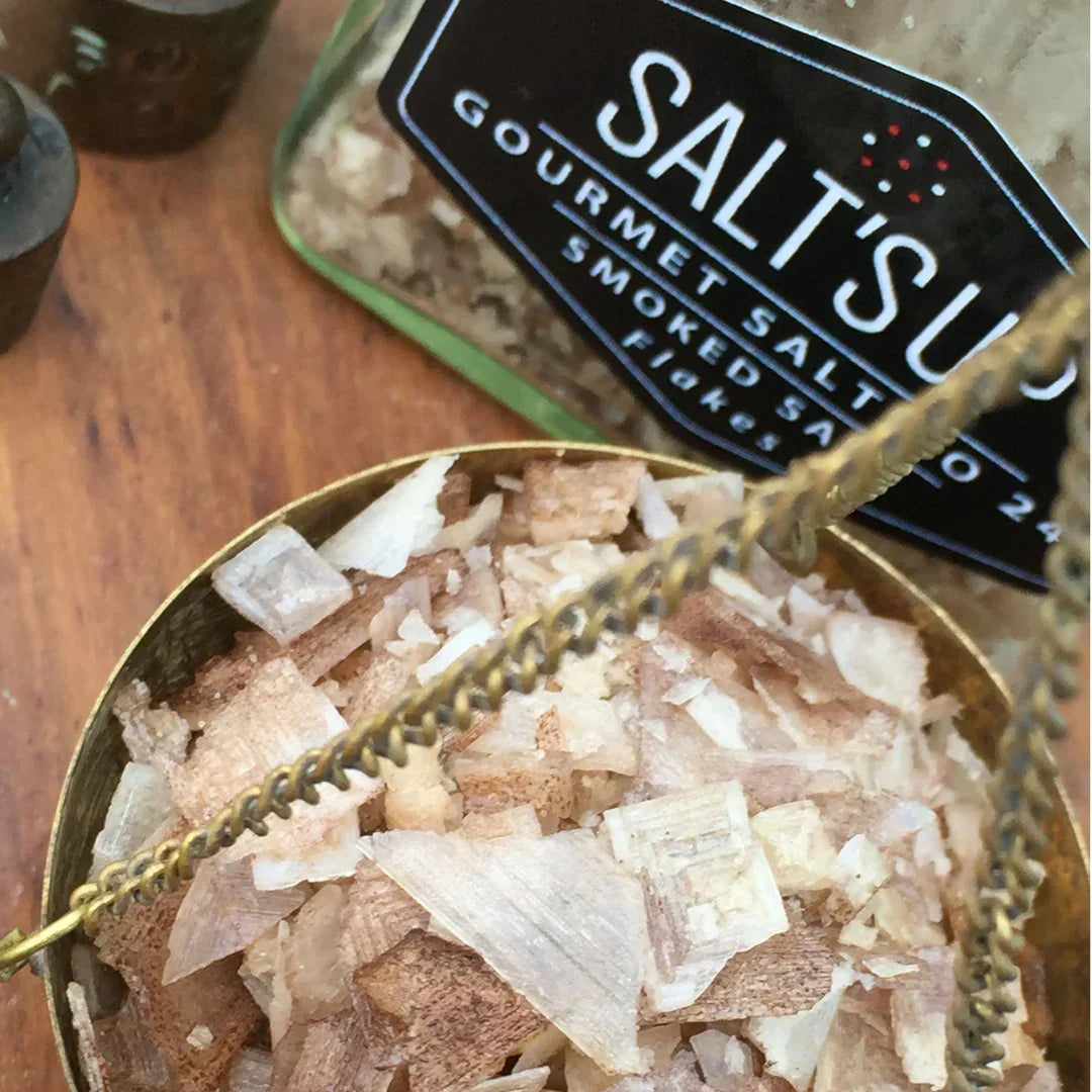 Close-up of gourmet smoked sea salt flakes in a brass container and glass jar