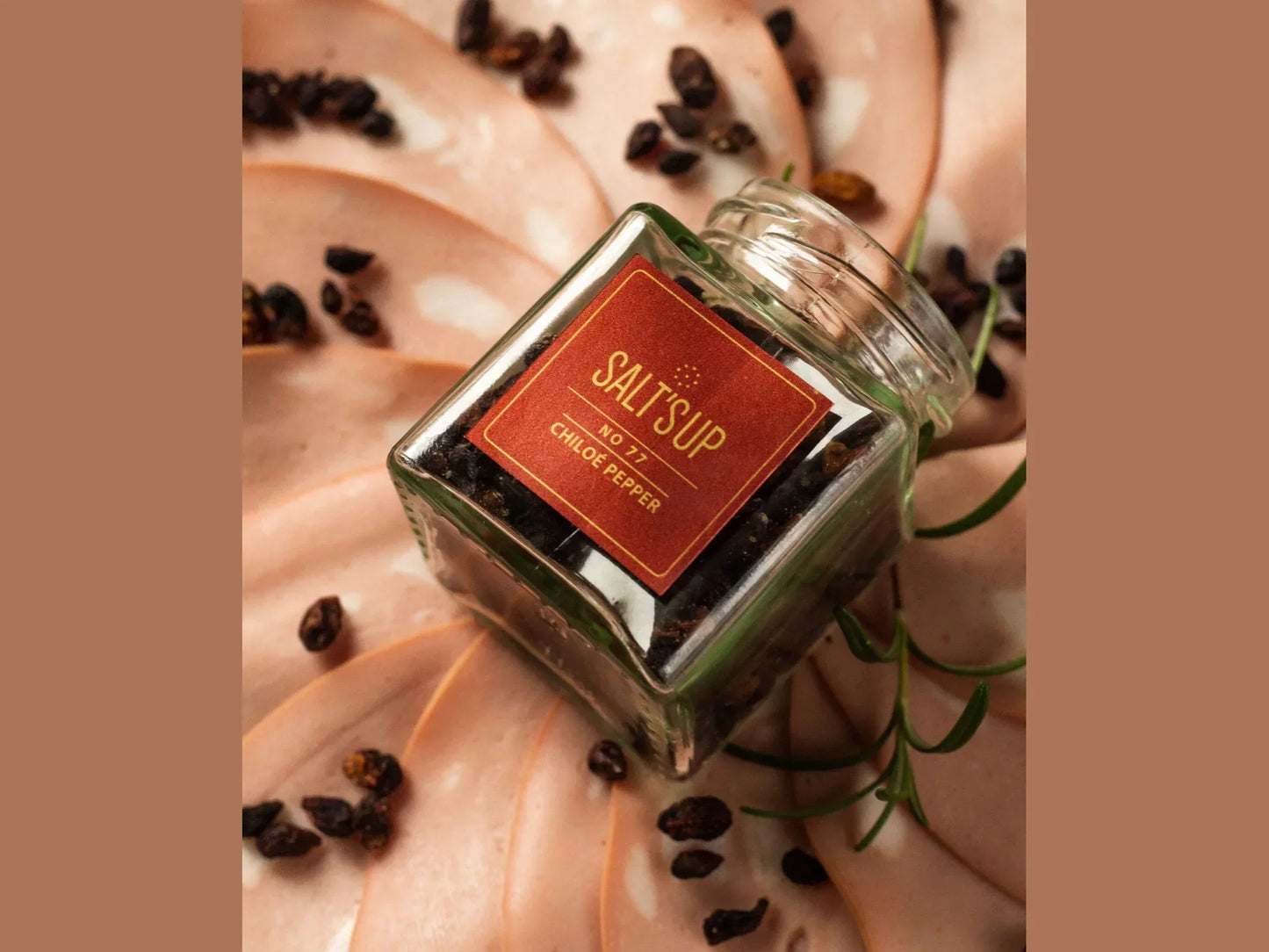 Glass jar of wild Chiloe pepper on sliced deli meat, artisan spice presentation