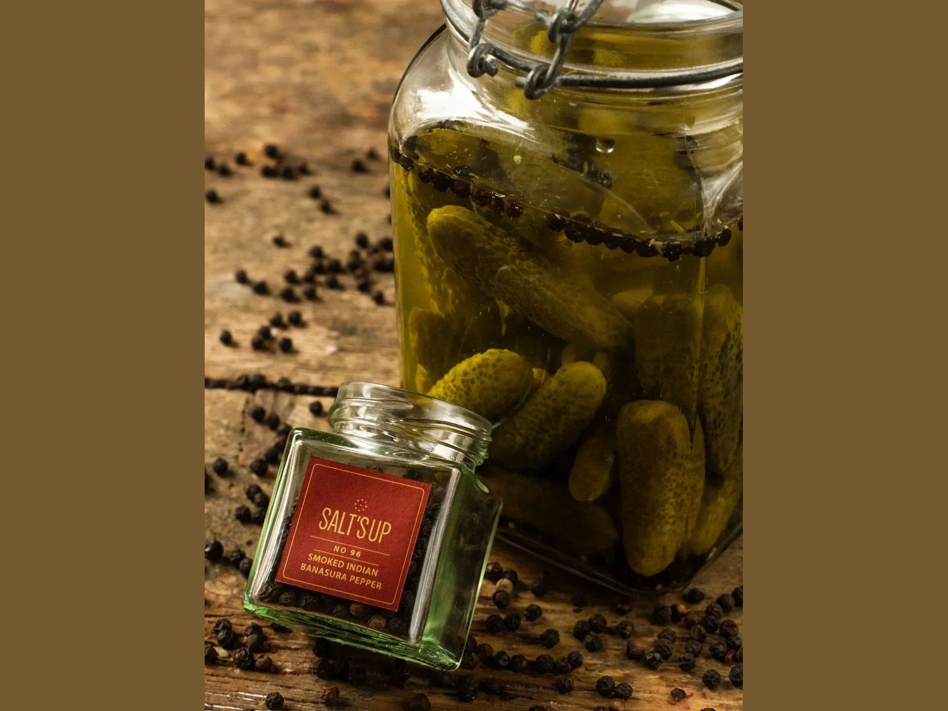 Glass jar of pickles with black peppercorns and smoked Indian pepper jar on rustic wooden table