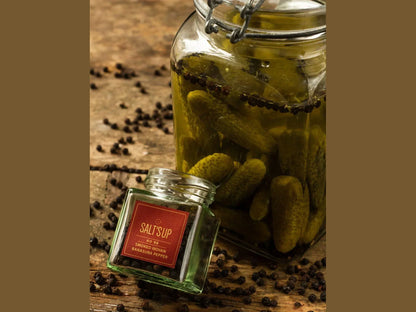 Glass jar of pickles with black peppercorns and smoked Indian pepper jar on rustic wooden table