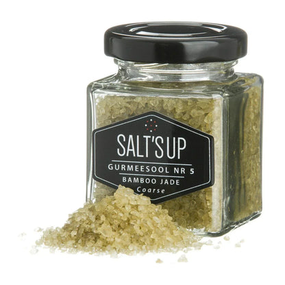 Glass jar of SALT'S UP Bamboo Jade coarse gourmet salt with some crystals spilled in front.