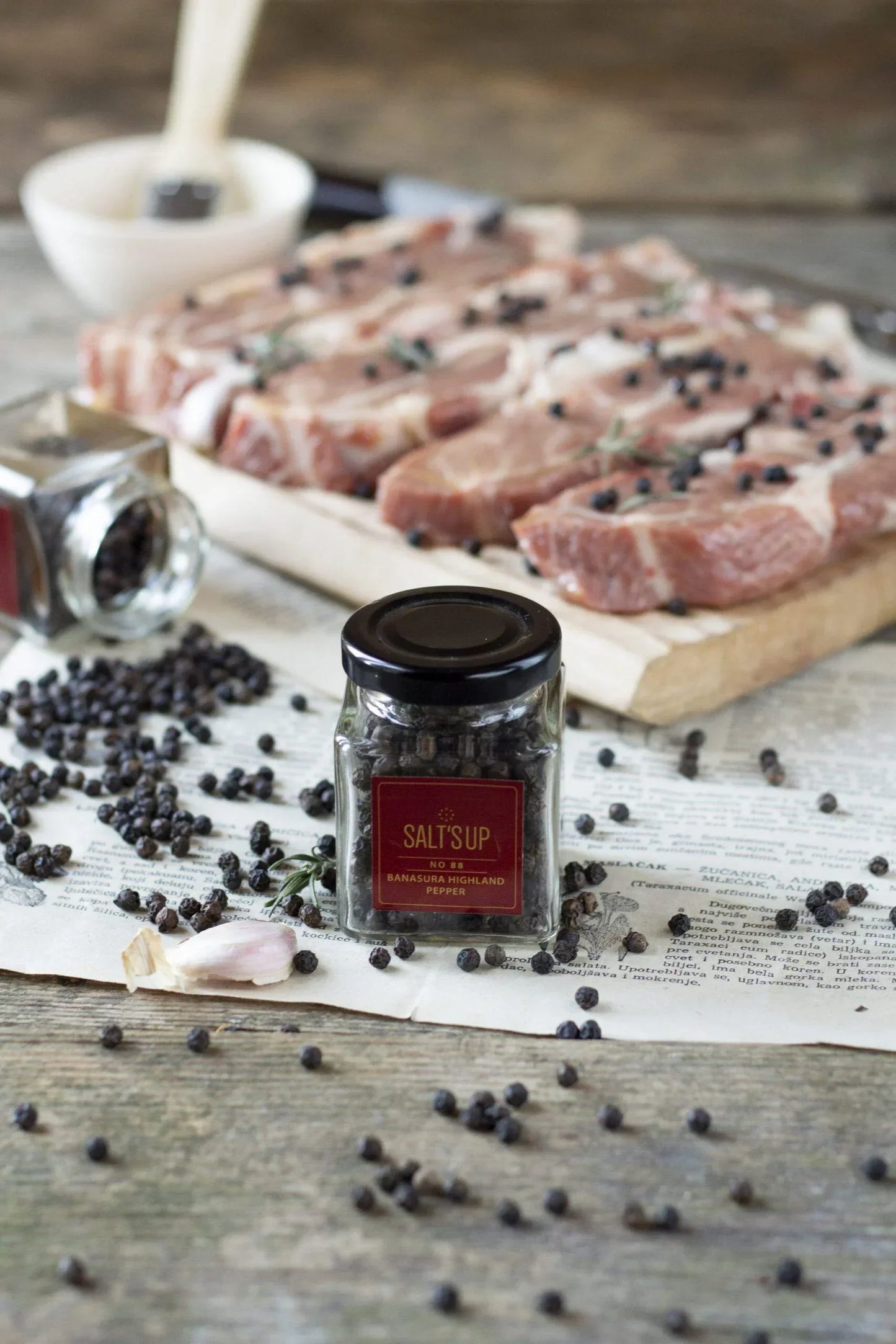 Banasura Highland pepper jar with black peppercorns and raw meat on rustic table, Spice n Slice Market