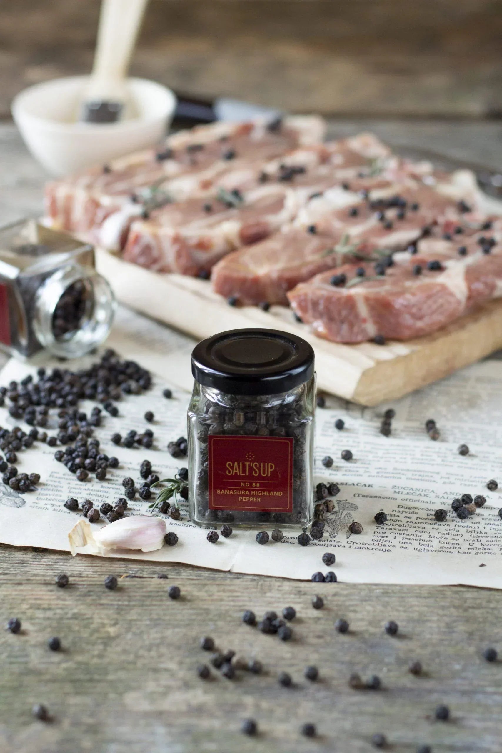Banasura Highland pepper jar with black peppercorns and raw meat on rustic table, Spice n Slice Market