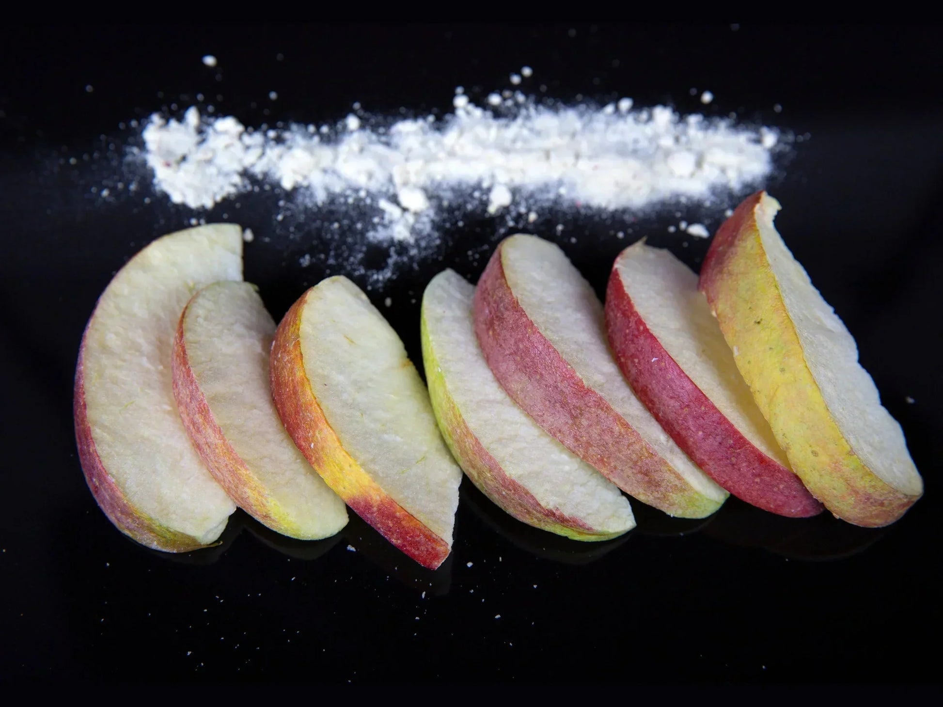 Sliced dried apple pieces with apple powder on a black background
