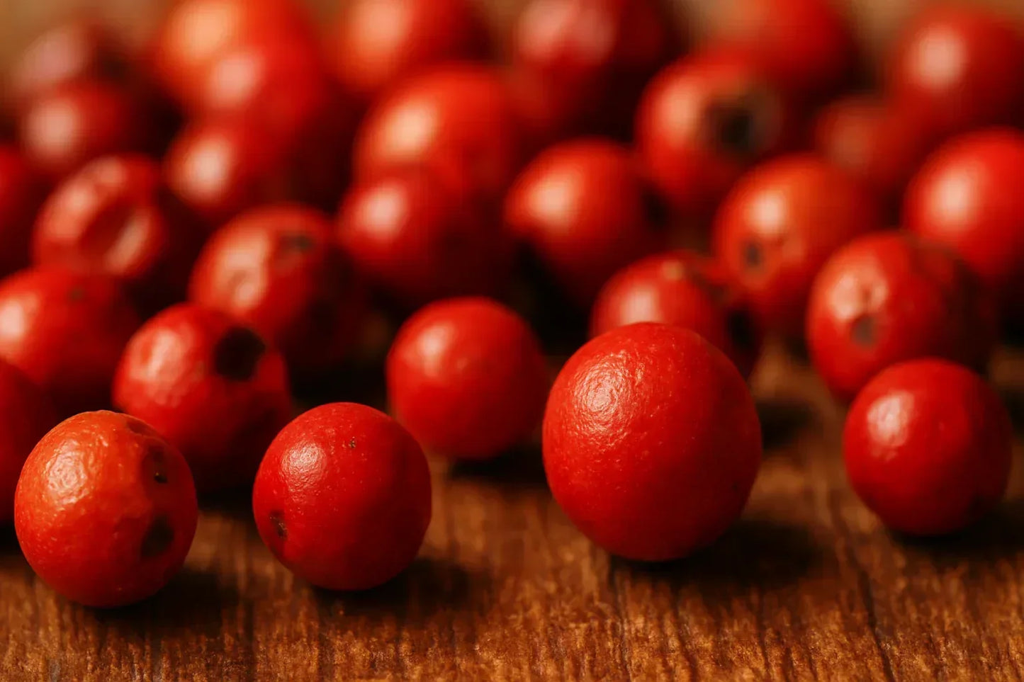 Close-up of whole red peppercorns on a rustic wooden surface, macro spice detail