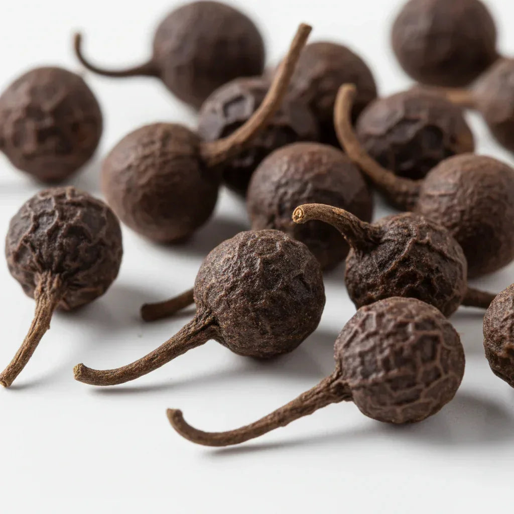 Close-up of whole cubeb peppercorns with distinctive tails on a white background