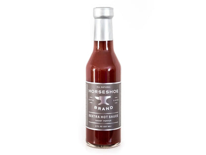 Ghost pepper hot sauce in clear glass bottle with silver label and cap on white background