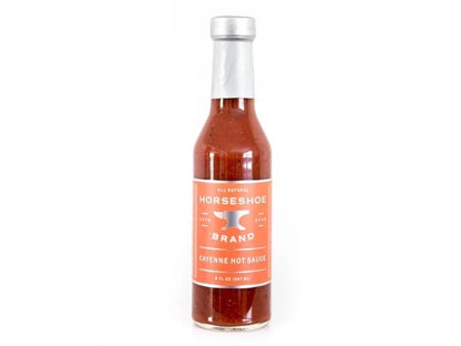 Glass bottle of Horseshoe Brand cayenne hot sauce with orange label on white background
