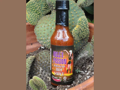 Habanero hot sauce bottle labeled Hell's Passion in front of potted cactus