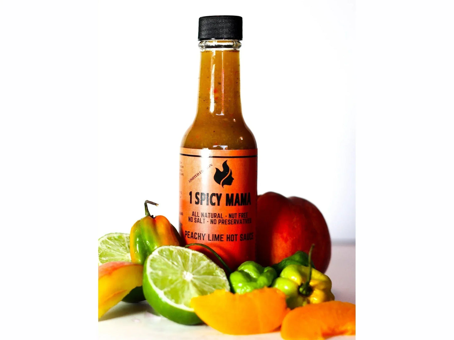 Peachy lime hot sauce bottle with fresh lime, peach, and peppers on white background