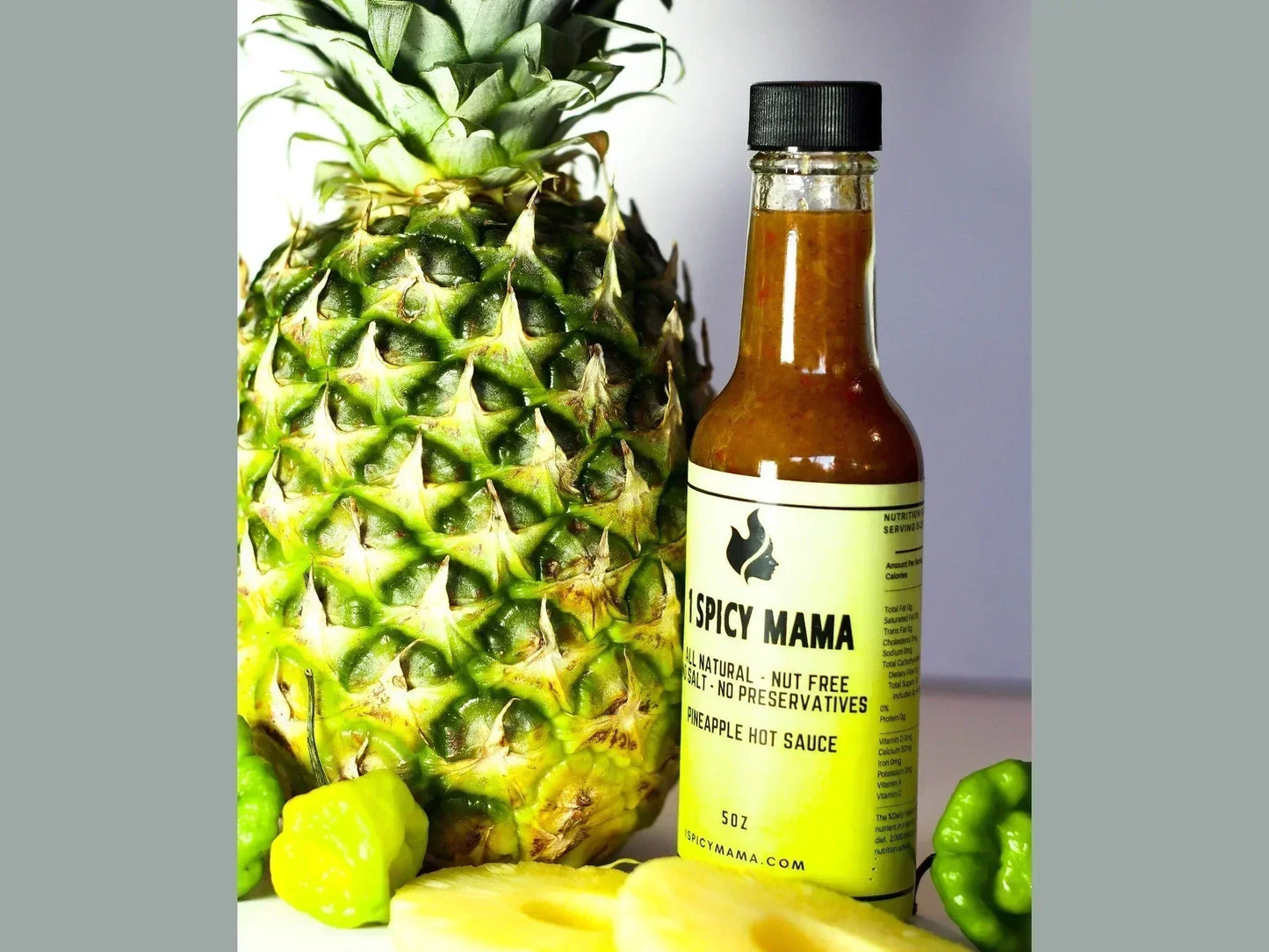 Pineapple, habanero peppers, and a bottle of pineapple hot sauce on a white surface