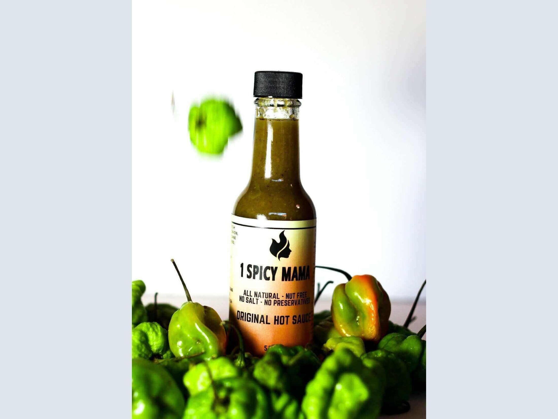 Original hot sauce bottle surrounded by fresh green peppers on white background