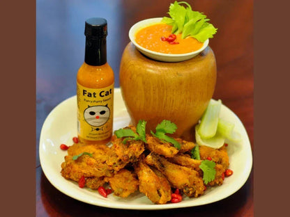 Plate of spicy chicken wings with hot sauce bottle, dipping sauce, and fresh herbs