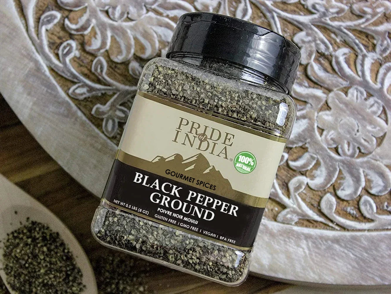Jar of ground black pepper with visible pepper grains on a decorative wooden surface