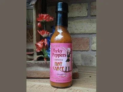 Bottle of Perky Peppers chipotle hot sauce on wooden surface, rustic brick background