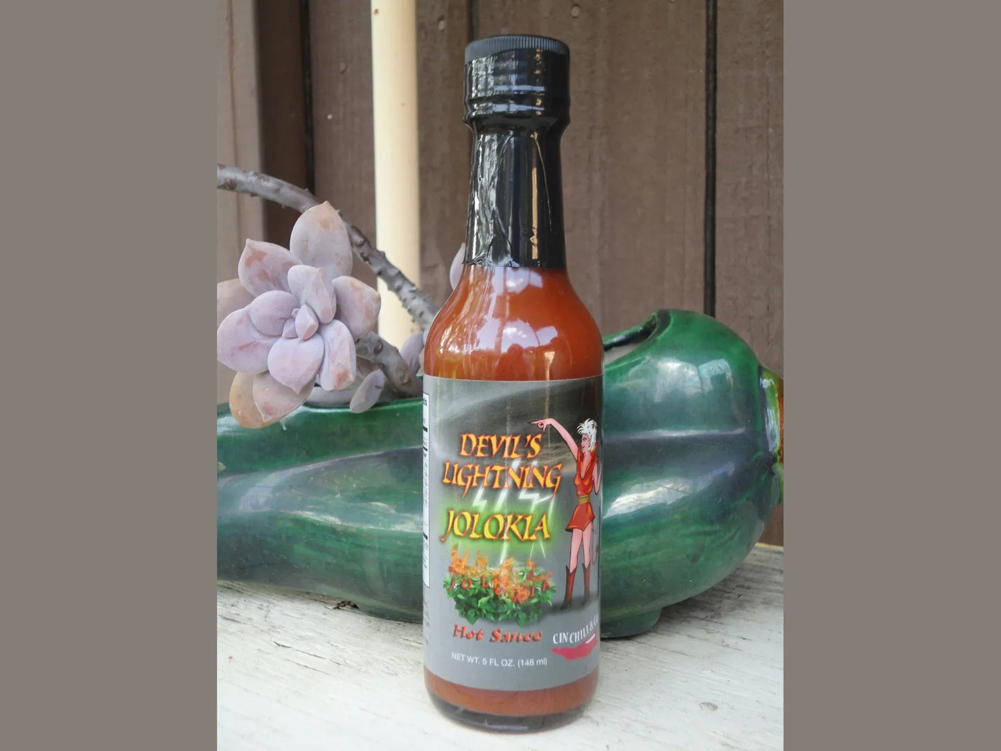 Devil's Lightning Jolokia hot sauce bottle on rustic table with succulent and green ceramic decor