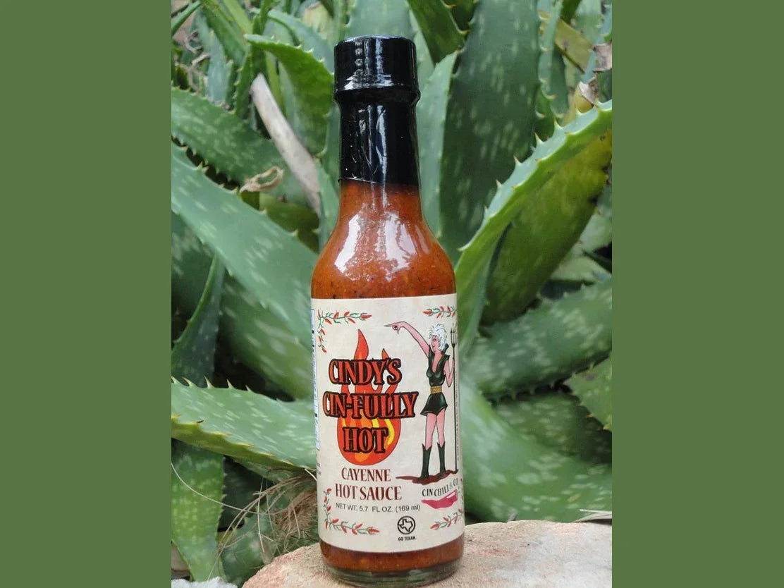 Bottle of cayenne hot sauce set outdoors among green aloe plants